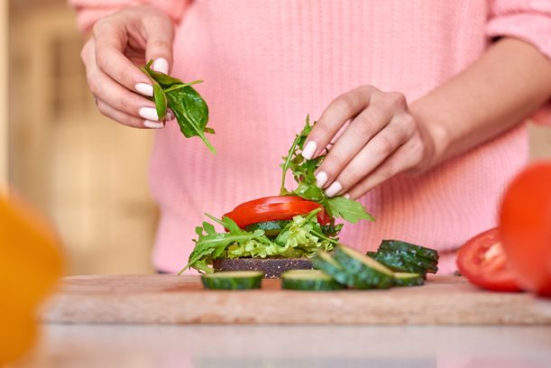 Woman hands making a healthy sandwich. Vegetables in shallow focus on foreground. Cucumbers and tomatoes